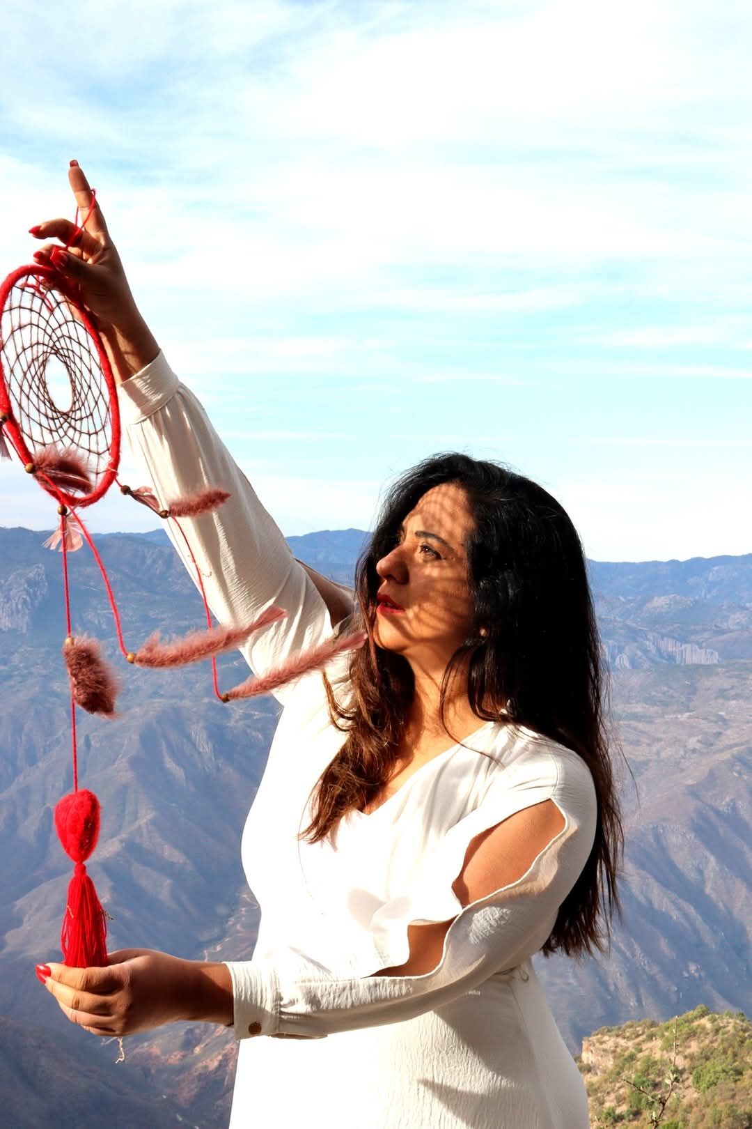 Victoria Arce sostiene un atrapasueños rojo frente a un paisaje de montaña